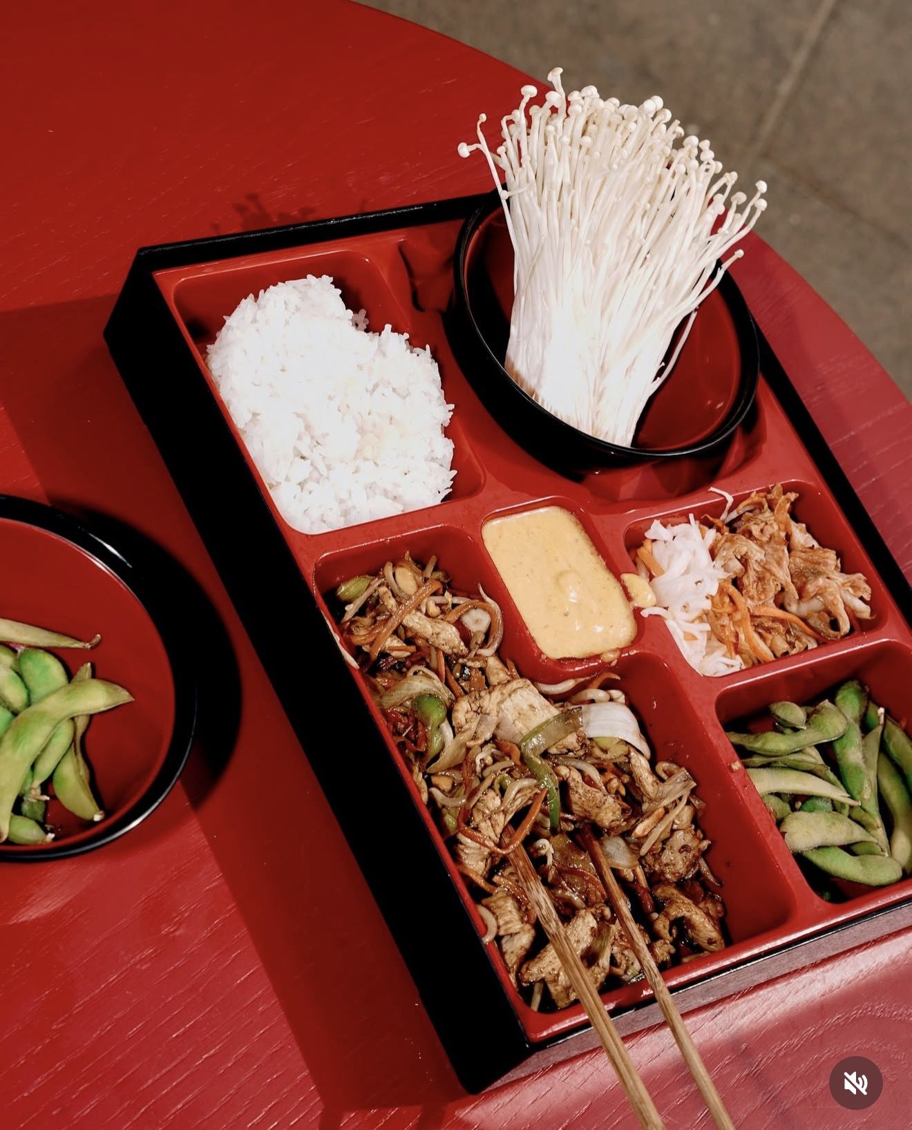 Red lacquer bento box with rice, chicken, edamame and enoki
