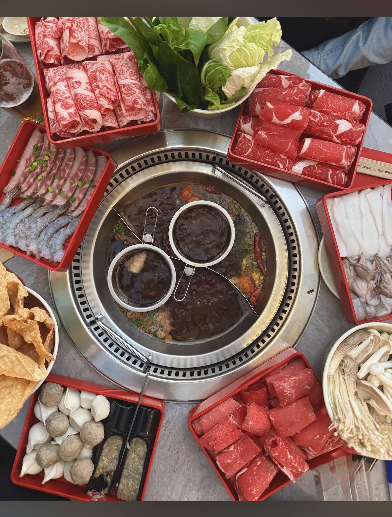 Split hot pot with plates of meat and dumplings around it